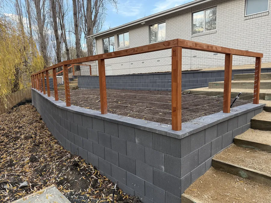 Curved block retaining wall topped with a timber and cable balustrade beside new steps