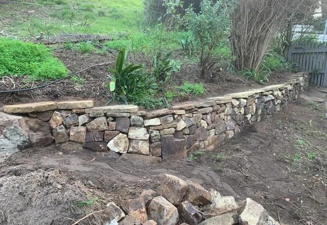 Hand-laid dry-stacked stone retaining wall curving around a garden bed