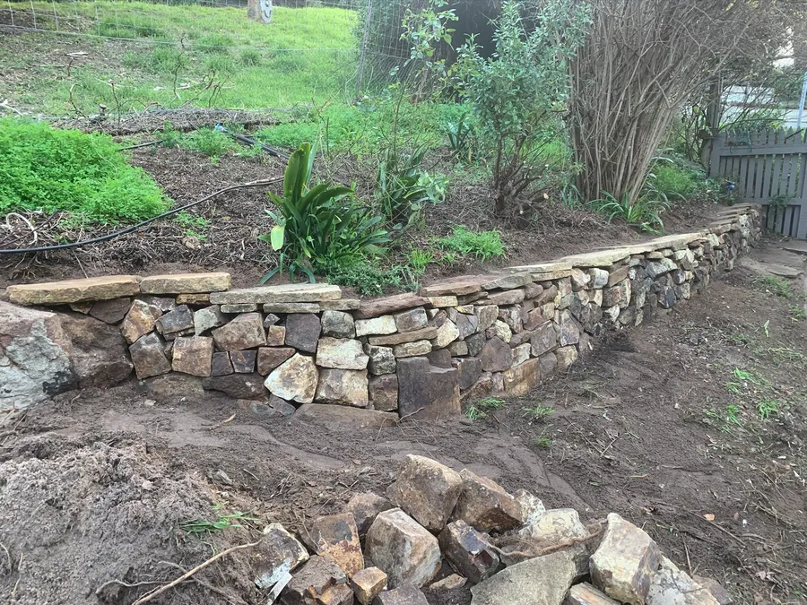 Dry-stacked stone retaining wall curving around a garden bed