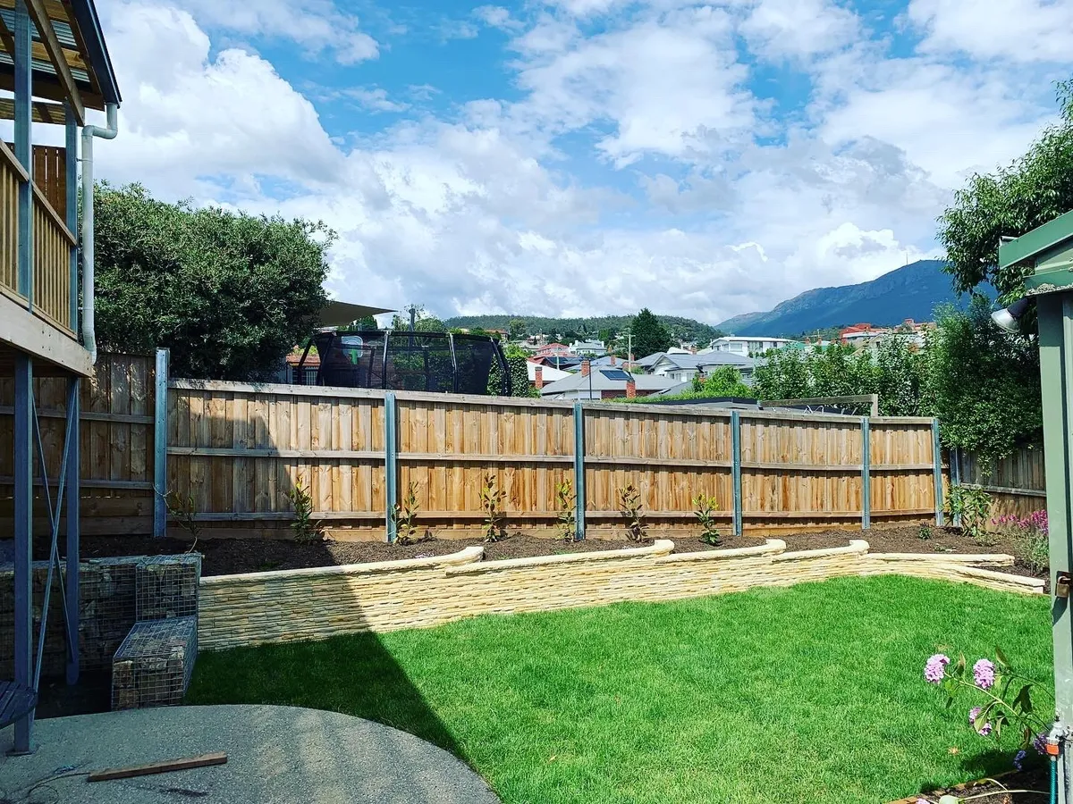 Freshly laid lawn beside a low sandstone-block retaining wall and new garden beds
