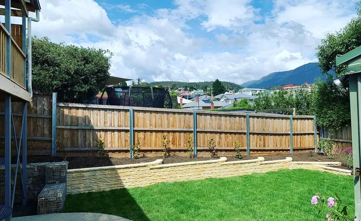 Freshly laid lawn beside a low sandstone-block retaining wall and new garden beds