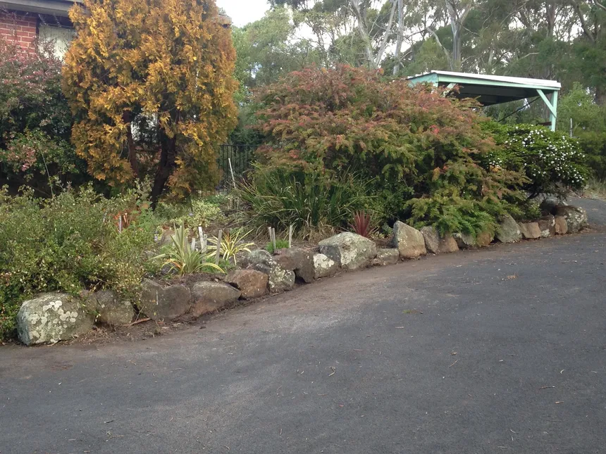 Neatly maintained mature garden with rock edging beside a driveway
