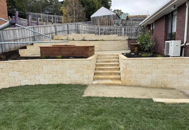 Sandstone-block terraces and steps rising from a fresh new lawn, with timber raised garden beds