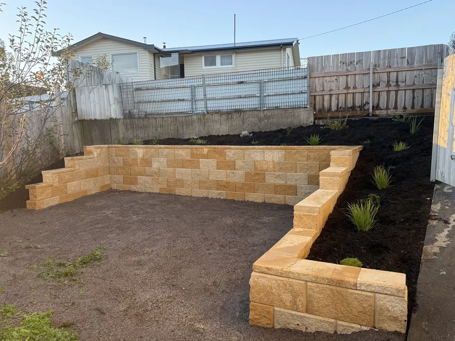 After: the sandstone-block wall wrapping the levelled yard, bank mulched and planted above